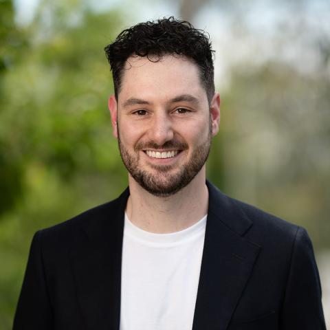 Profile picture of Robert Holian, Greens Candidate for Greater Bendigo City Council Lockwood Ward By-election. Robert is standing in front of blurred out trees and parkland. Robert is wearing a dark blazer with a white shirt.